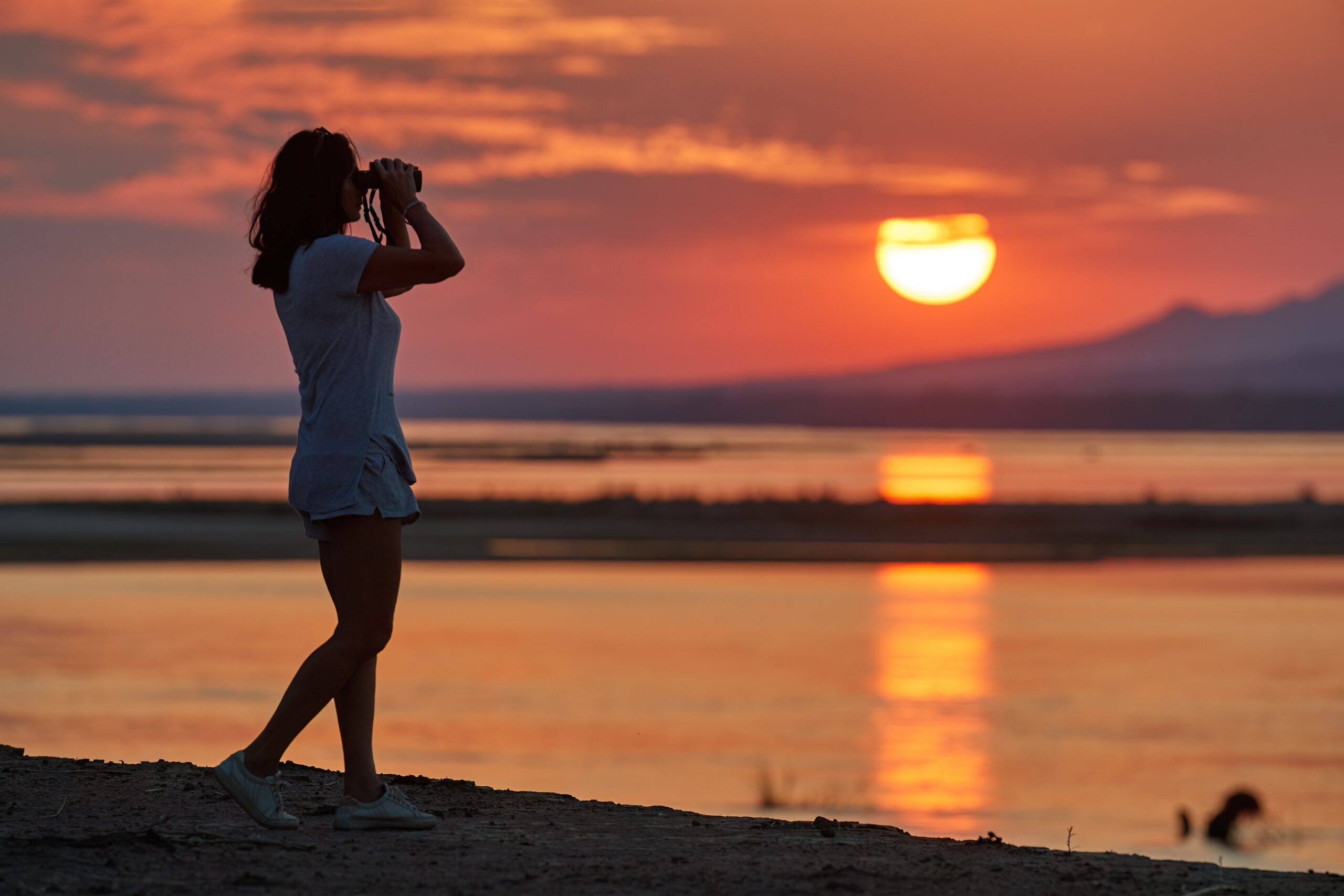 Silhouet van een vrouw met verrekijker aan de oever van de Zambezi in Zimbabwe tijdens zonsondergang – safari met Christoffel Travel