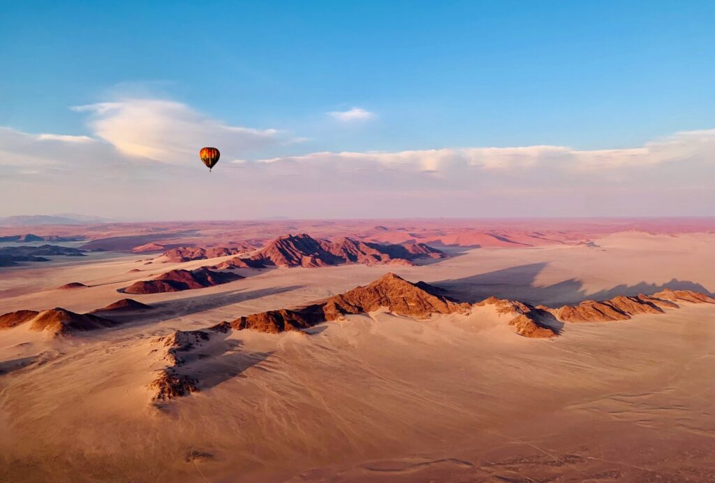 Luchtballon zwevend boven de oranje zandduinen van de Namibwoestijn bij zonsopkomst – Christoffel Travel.