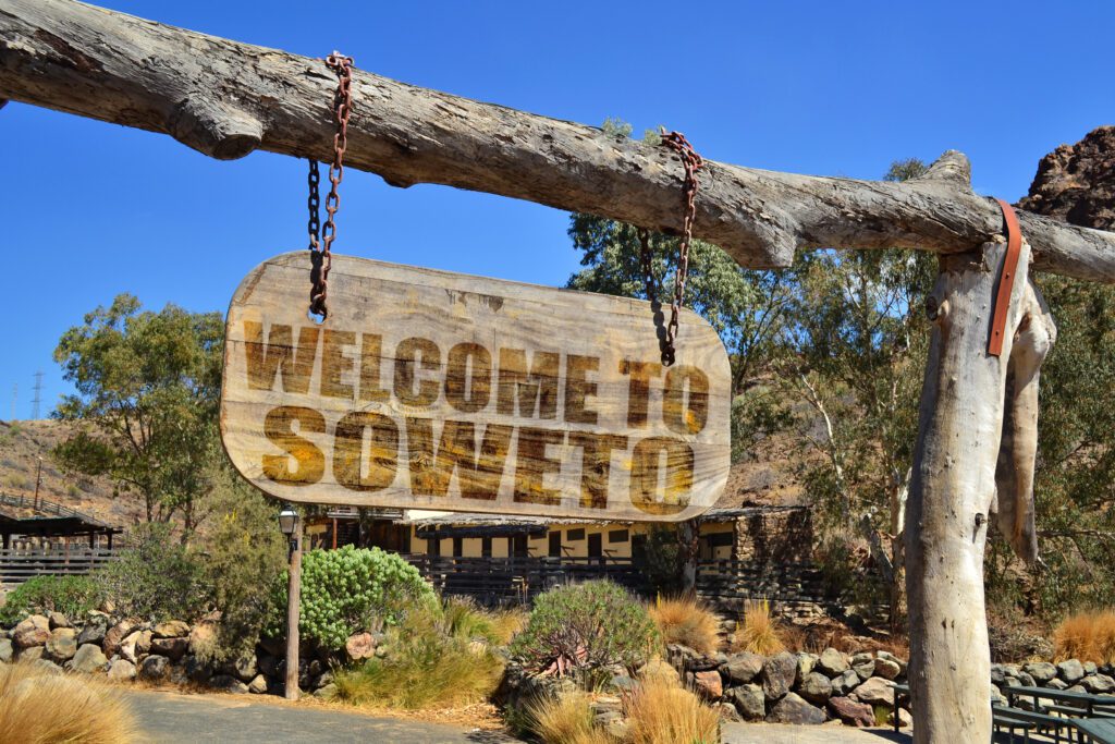 Oud houten vintage welkomstbord met de tekst "Welcome to Soweto", hangend aan een tak – Christoffel Travel.